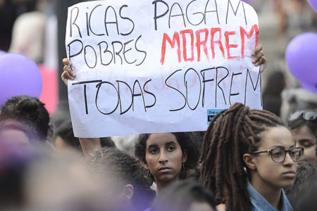 A woman holds a sign in Brazil which reads, “Rich women pay, poor women die, all suffer” (Photo: Fernando Frazão/Agência Brasil)