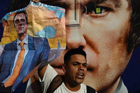 A supporter of Sergio Massa holds a poster with an image of the Peronist candidate during a campaign event for Javier Milei (pictured in the background) - Luis Robayo/AFP
