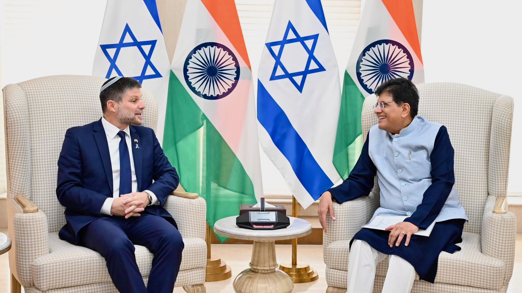 Israeli finance minister and Indian minister of commerce and industry sit in front of Indian and Israeli flags.
