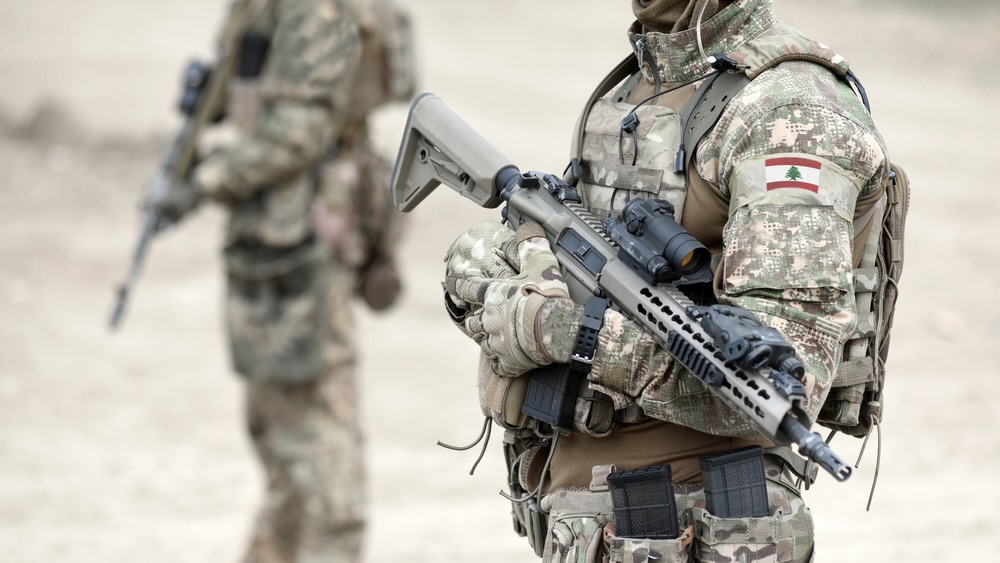 Lebanese soldier holds assault rifle and flag of Lebanon on military uniform.