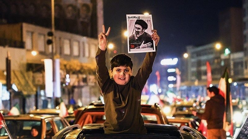 Boy holds up picture of new Supreme Leader Ayatollah Seyed Mojtaba Khamenei while raising the victory sign