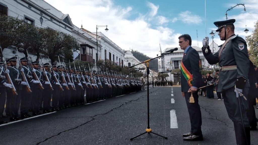 Rodrigo Paz stands in front of microphone in front of row of soldiers with muskets